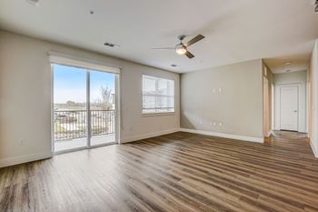 A room with a sliding glass door leading to a balcony, hardwood floors, and a ceiling fan.